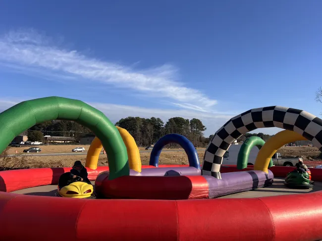 Inflatable go-kart track with colorful arches and riders on toy cars under a blue sky.