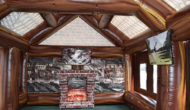 Inflatable room with brick fireplace and mounted TV screens inside a wooden log cabin design.