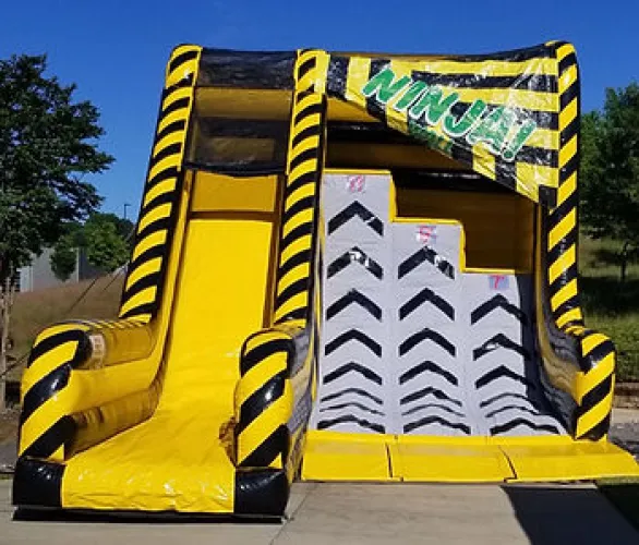 Yellow and black inflatable Ninja Warrior obstacle course with climbing steps and slide outdoors.