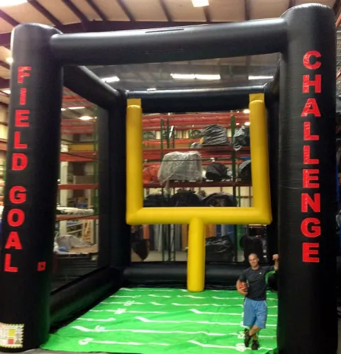 Indoor inflatable field goal challenge game with a man holding a football, standing on green field mat.