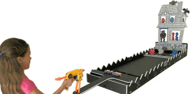 Girl playing a tabletop shooting game with a toy gun aiming at targets on a haunted house setup.