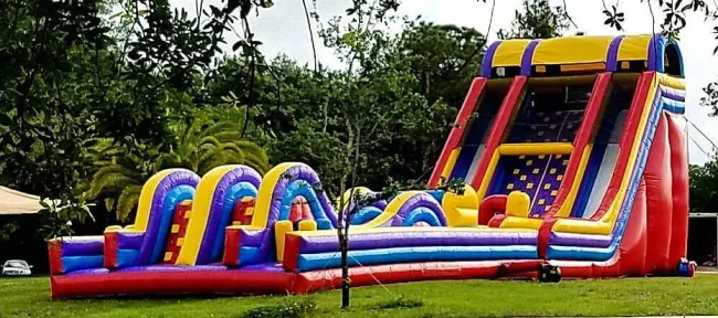 Colorful inflatable obstacle course with climbing wall and slides set up on green grass outdoors.