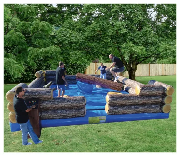 People playing on an inflatable log rolling game with large logs surrounded by a soft blue surface outdoors.