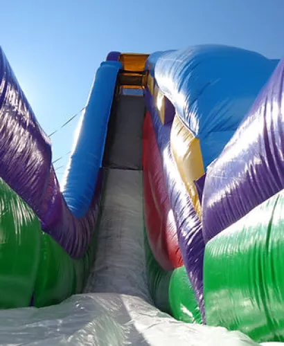Brightly colored inflatable slide with blue, purple, green, and red sections under clear sky.