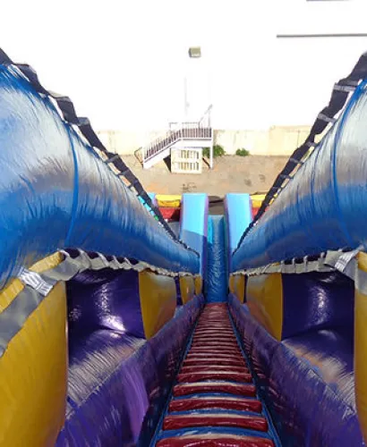 Colorful inflatable slide with blue, yellow, red, and purple sections viewed from the top looking down.