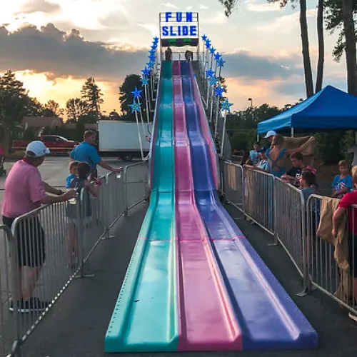 Colorful three-lane fun slide at fair with people waiting and sunset sky in background