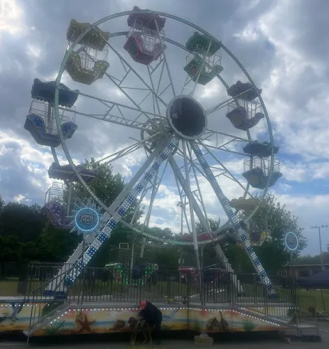 Ferris wheel with colorful cabins lit by LED lights at an outdoor carnival event under a cloudy sky.
