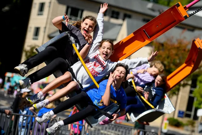 Children joyfully riding an outdoor amusement park swing ride on a sunny day with raised hands and smiles