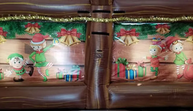 Christmas-themed inflatable decoration with elves, gifts, bells, and festive garlands on wooden background.