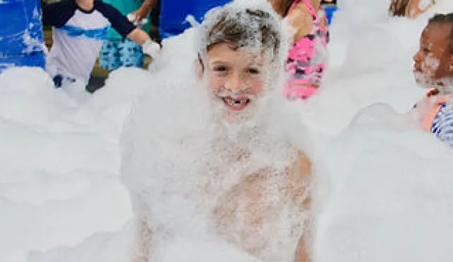 Happy children playing and covered in foam bubbles at an outdoor foam party on a sunny day