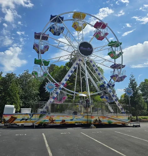 Colorful Ferris wheel with blue, yellow, red, green, and purple cabins under a sunny sky with scattered clouds.