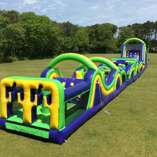 Long inflatable obstacle course in green, yellow, and blue set up on a grassy field with trees in the background