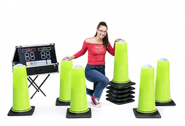 Smiling young woman with red glasses and outfit poses among tall green cones and electronic scoreboard on white background.