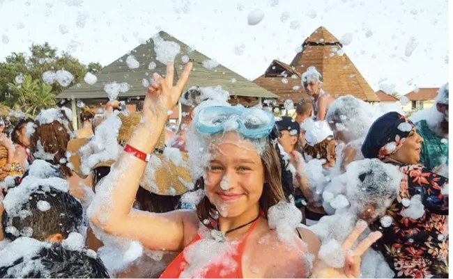 Smiling girl wearing goggles at a lively outdoor foam party with crowd and festive atmosphere.