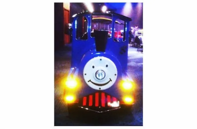 Front view of a blue train engine with a smiling face and bright yellow headlights indoors at night.