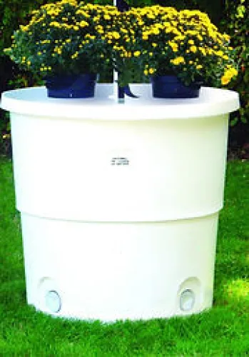 Large white rain barrel with yellow potted flowers on top sitting on green grass.