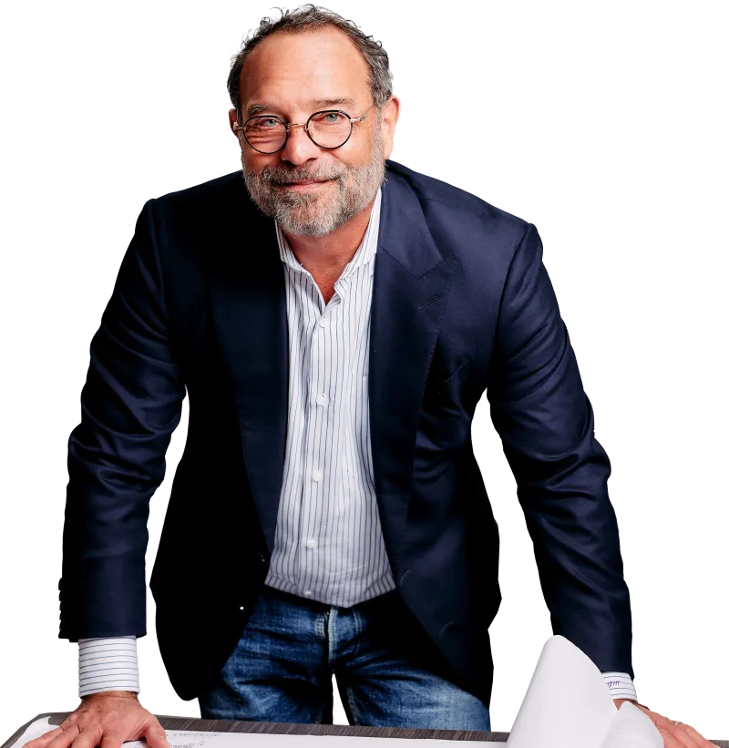 Middle-aged man in glasses and blazer leaning on table with blueprints