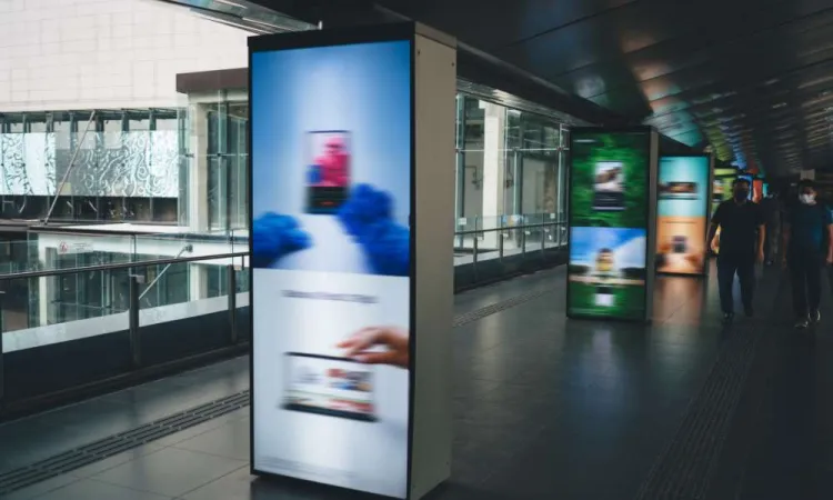 Blurry digital advertisement displays on pillars in a modern indoor pedestrian walkway with people walking.