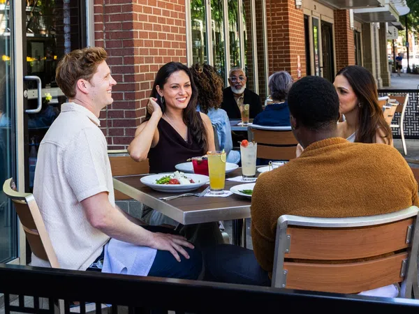 Group of friends enjoying drinks and food at outdoor tables outside Marlow's Tavern on a city sidewalk.