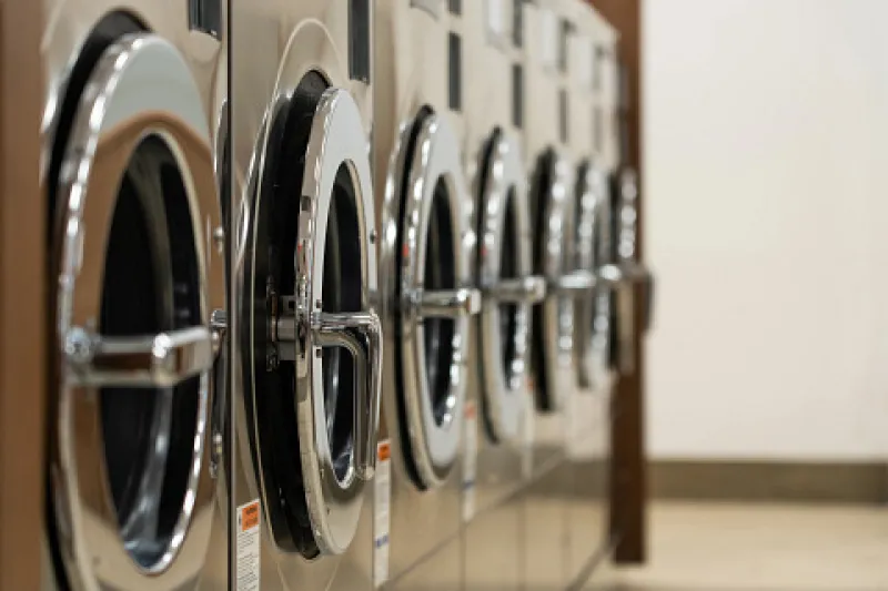 Row of stainless steel front-loading washing machines in a laundromat with reflective surfaces.