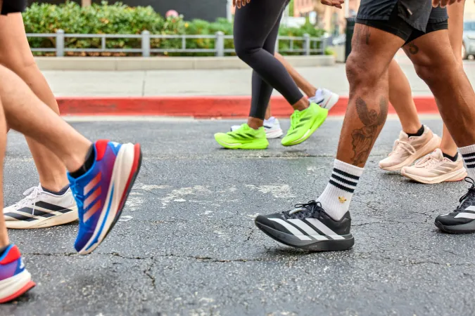 Close-up of diverse people walking on asphalt wearing colorful athletic shoes and socks in urban setting.