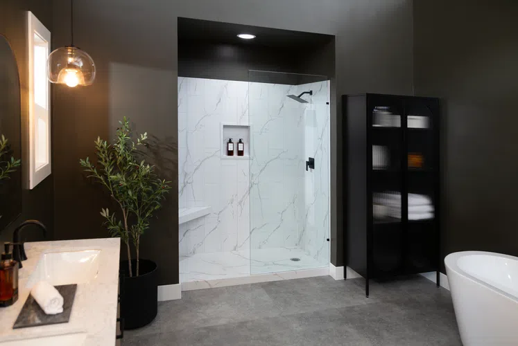 Modern bathroom with glass shower enclosure, white marble tiles, black fixtures, and minimalist decor.