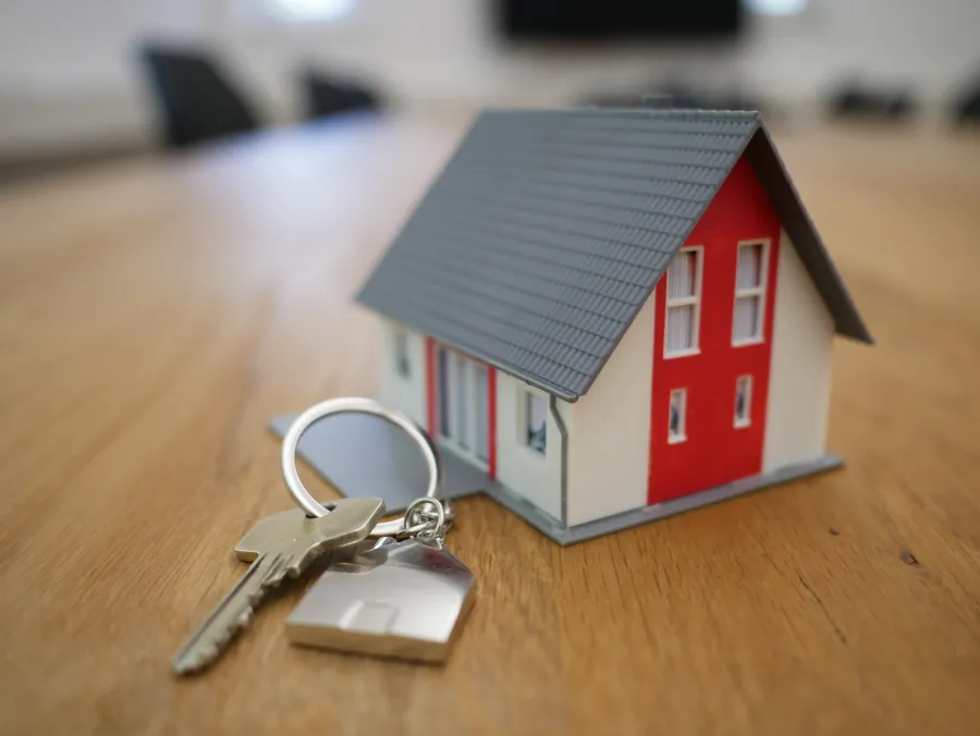 a key and model of a house sit on top of a wooden table