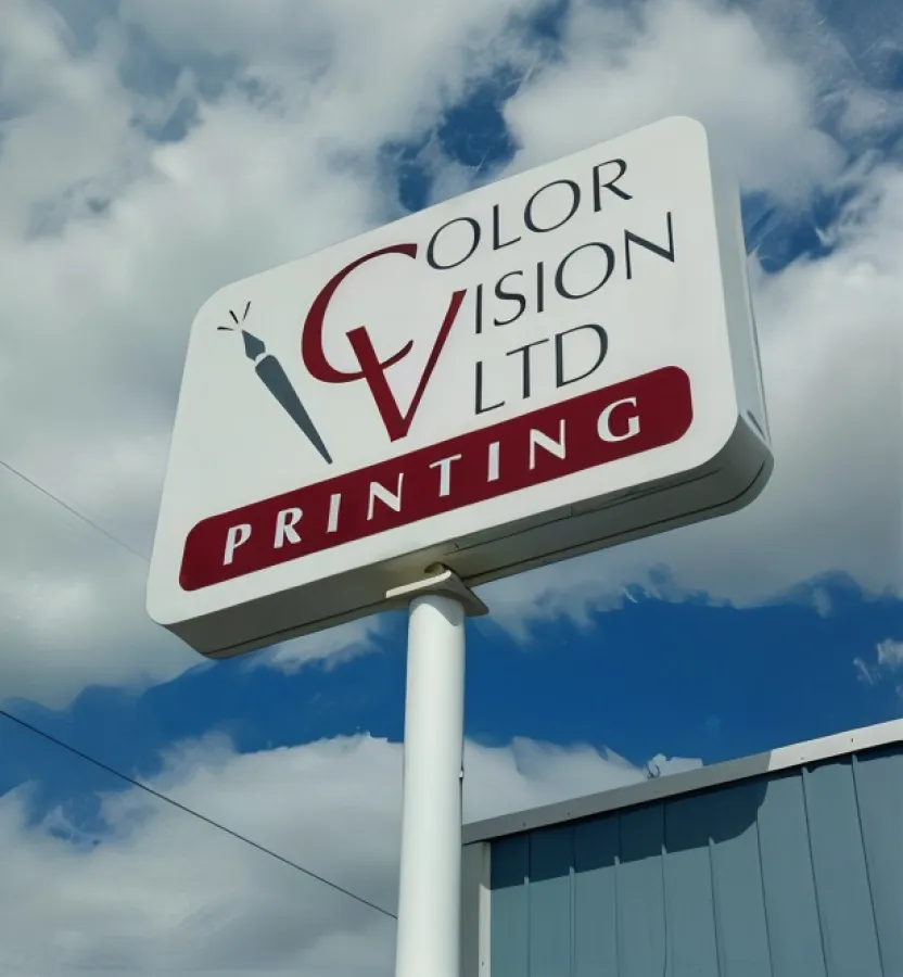 Color Vision Printing sign on pole against a partly cloudy blue sky background.