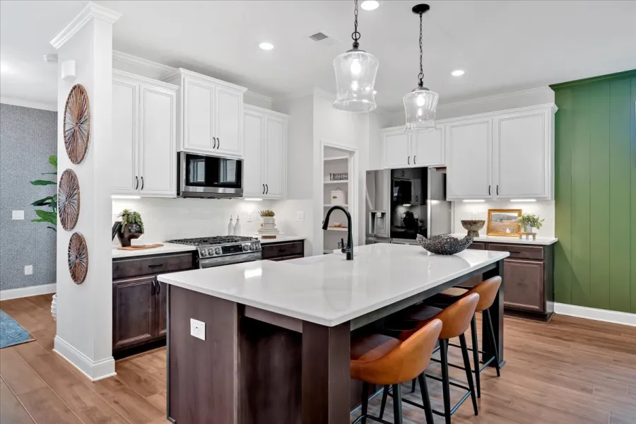 Modern kitchen with white and dark wood cabinets, large island, brown bar stools, and green accent wall.
