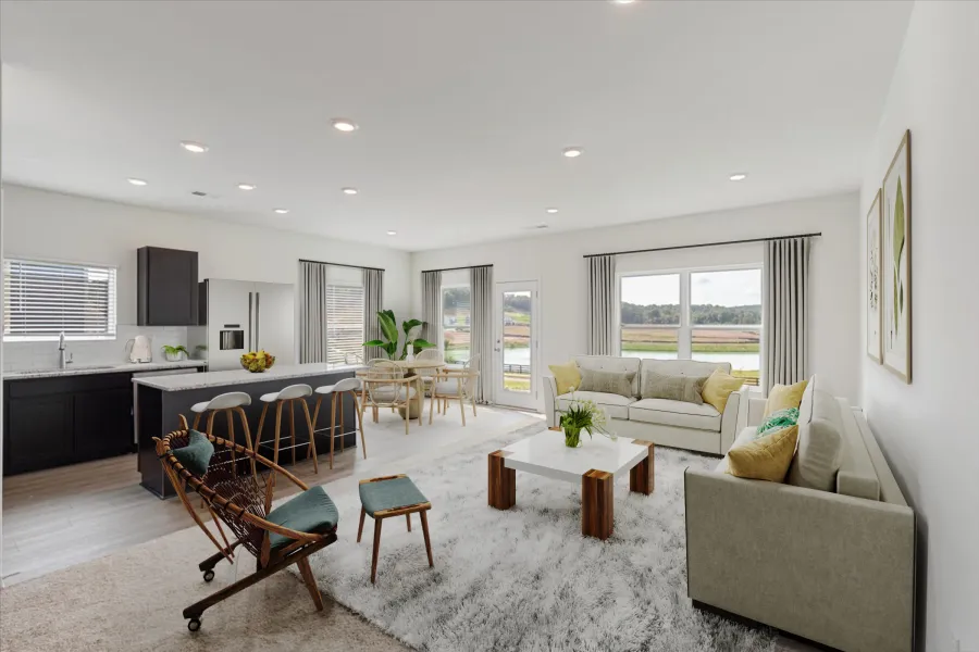 Bright open living room and kitchen with modern furniture, large windows, natural light, and neutral decor.