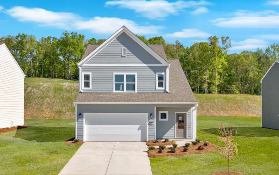 Two-story gray house with white trim, double garage, driveway, and small landscaped front yard under a blue sky.