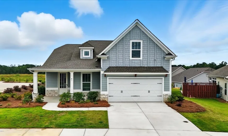 Modern two-story gray house with a two-car garage, neatly landscaped lawn, and a cloudy blue sky background