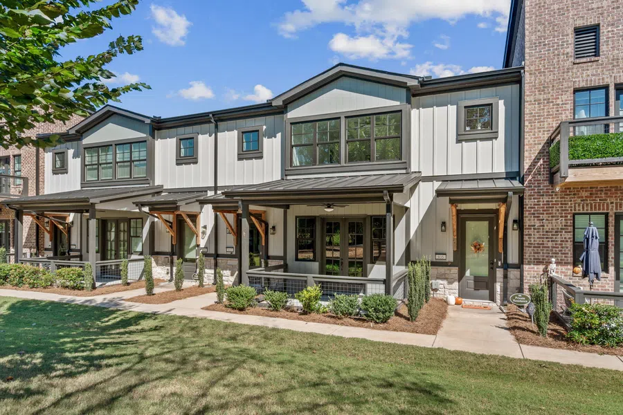 Modern townhouses with white panel siding, large windows, front porches, and landscaped yards under a blue sky