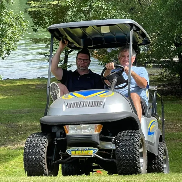 a couple of men in a golf cart by a river