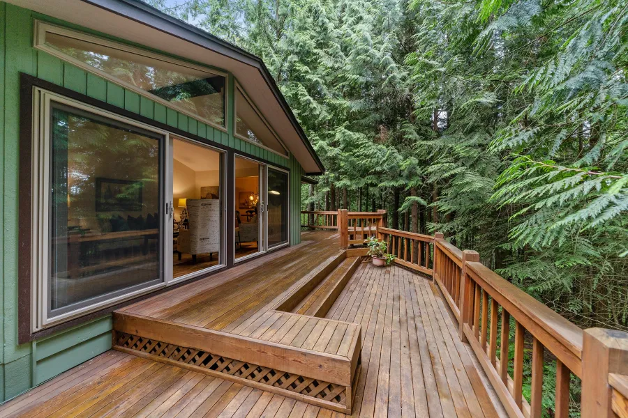 a wooden deck with a glass door and a wood railing with trees in the background