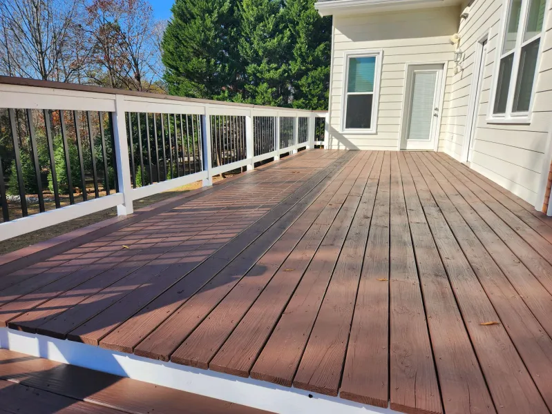 a deck with a wood railing and a house in the background