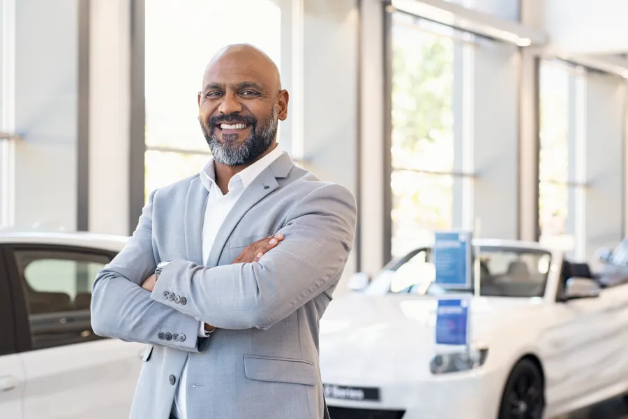 a car dealership owner smiling next to a car for sale