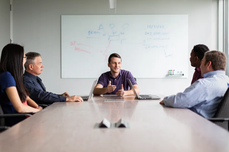 a group of people sitting at a table in front of a whiteboard