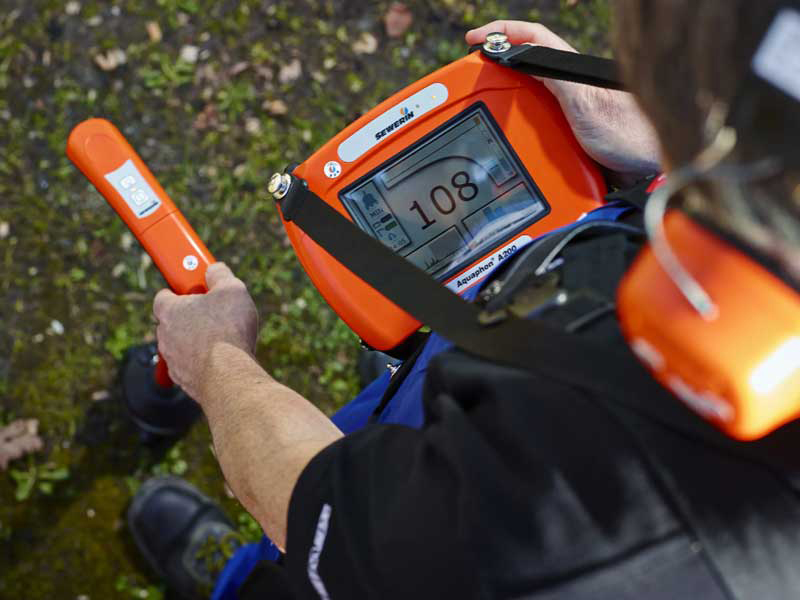 Technician wearing headphones and using an acoustic leak detection receiver and ground microphone to listen for an underground water leak