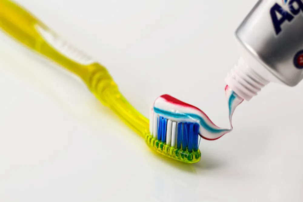 Yellow toothbrush with blue and white bristles being ap
