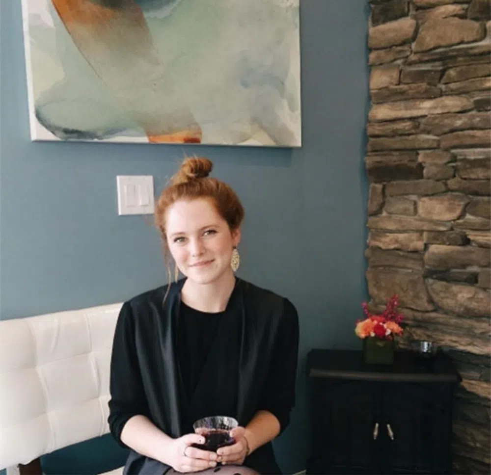 Young woman with red hair sitting indoors holding a glass of red wine
