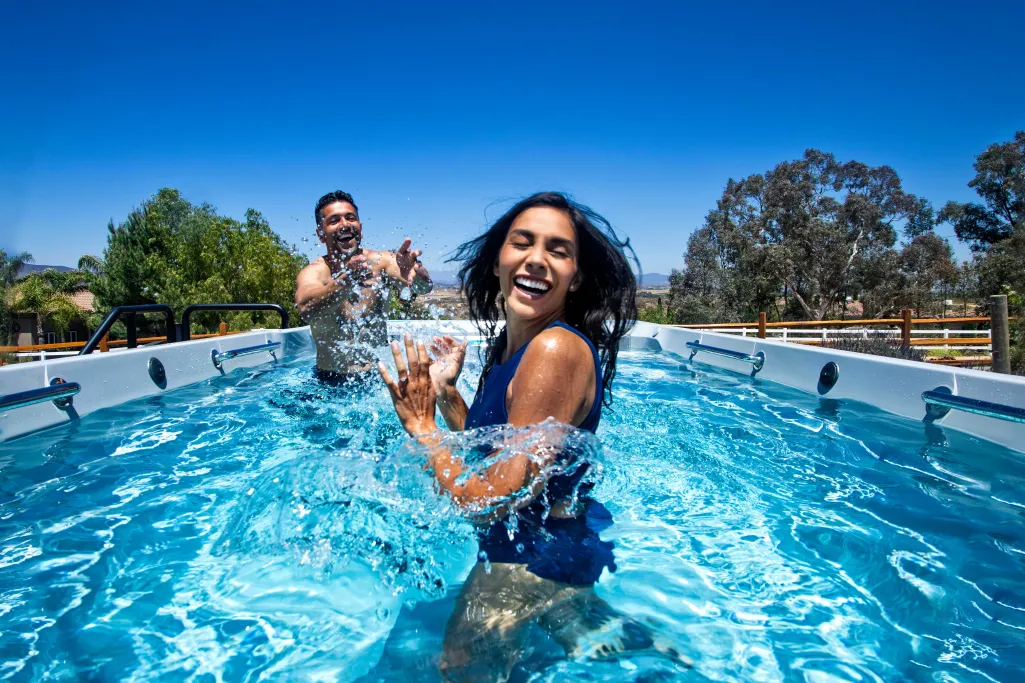 Happy young couple splashing water and enjoying time in an above ground pool on a sunny day.