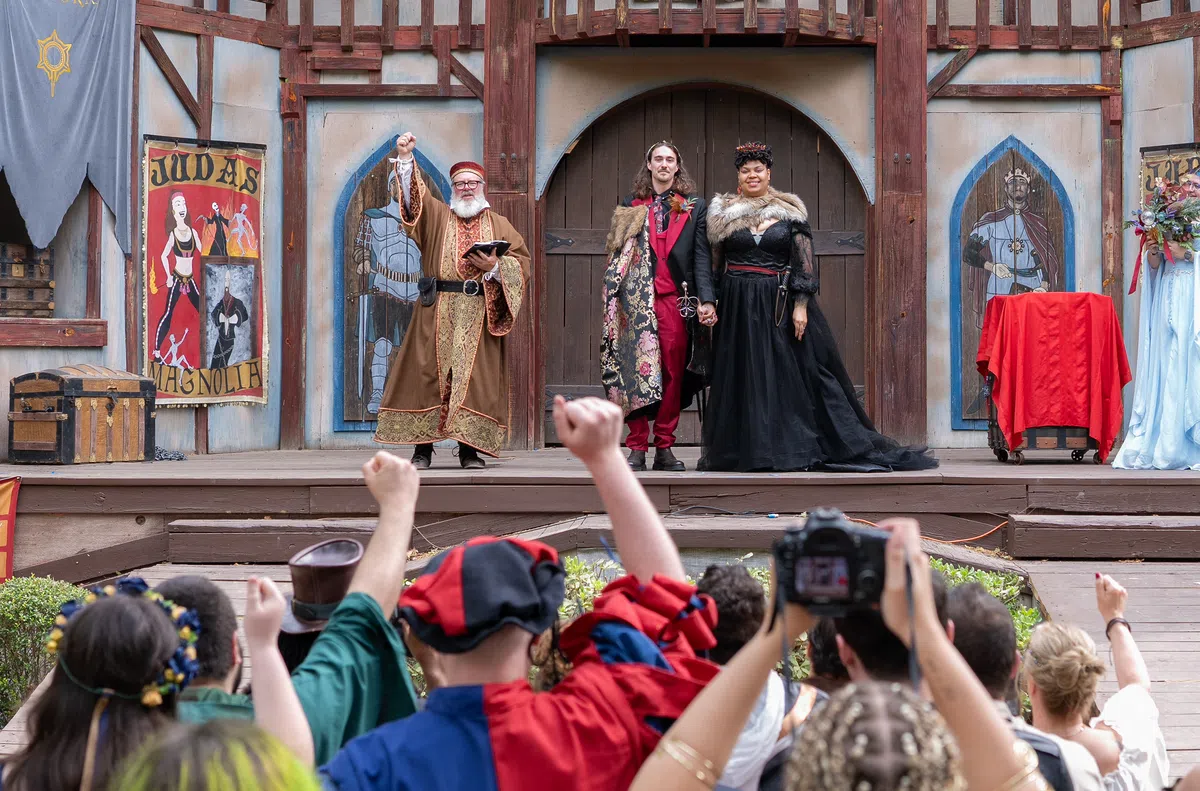 A couple stands on stage with the Festival officiant for their handfasting ceremony