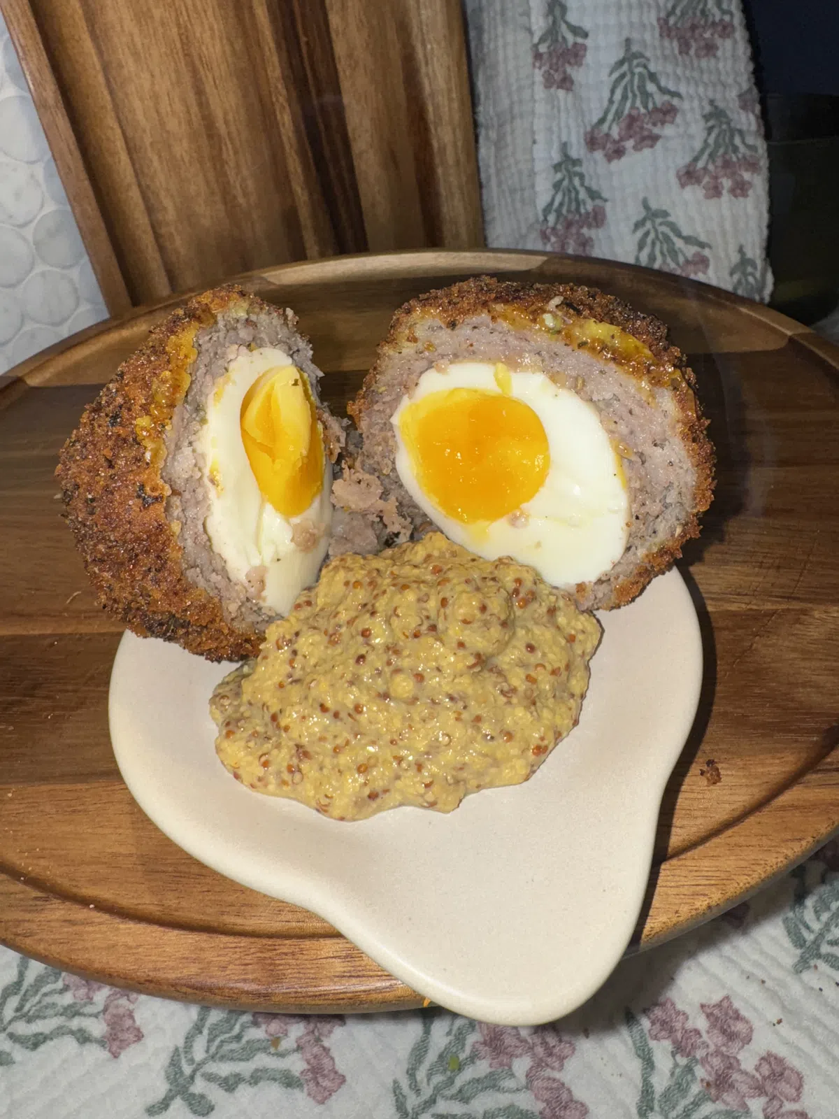 A Scotch egg cut in half, soft yolk showing, with grainy mustard