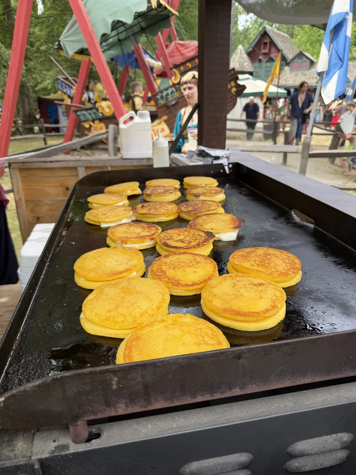 Arepas browning on a griddle with the pirate ship ride behind