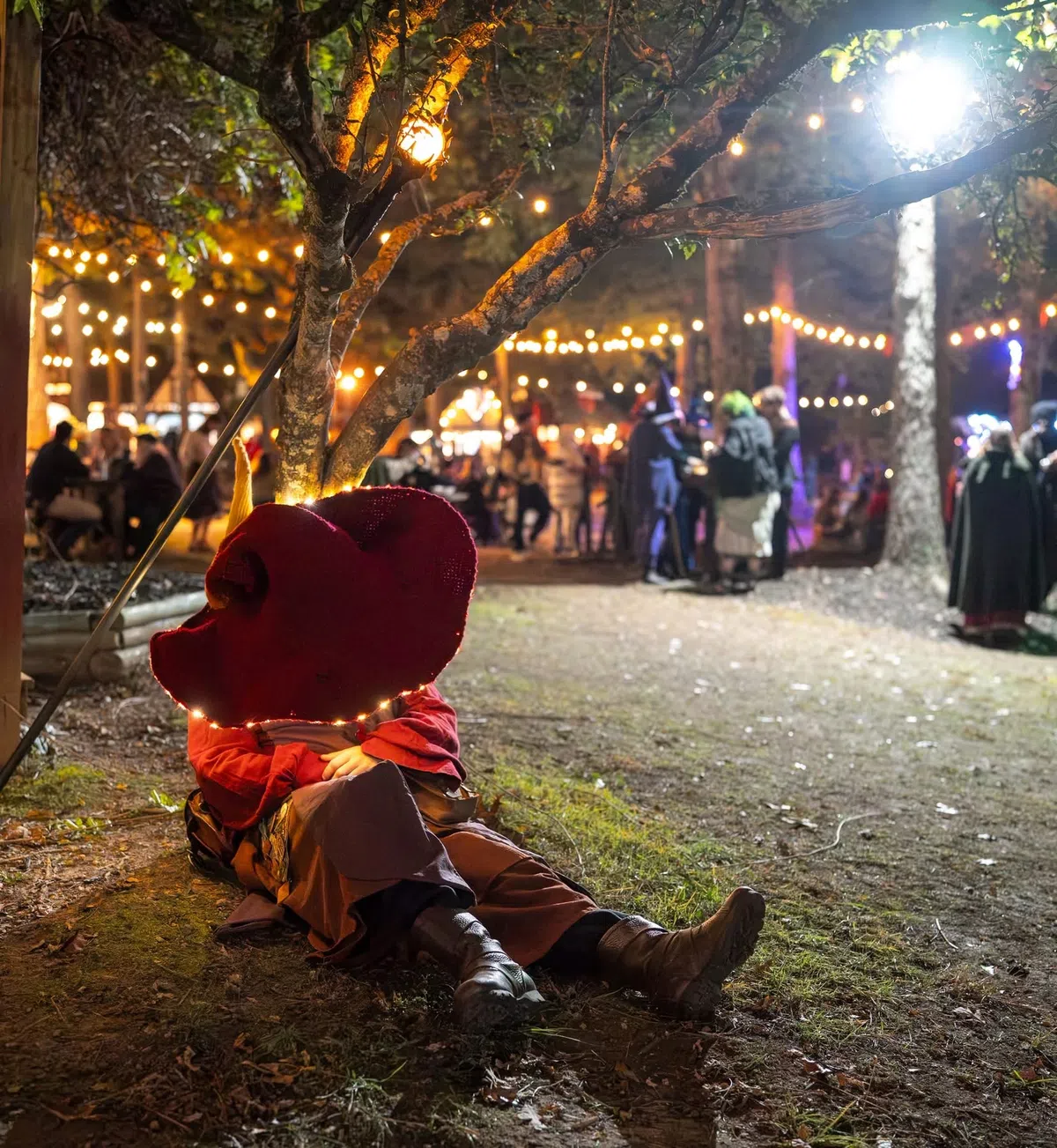 A wizard character resting beneath strings of lights at the Festival after dark.