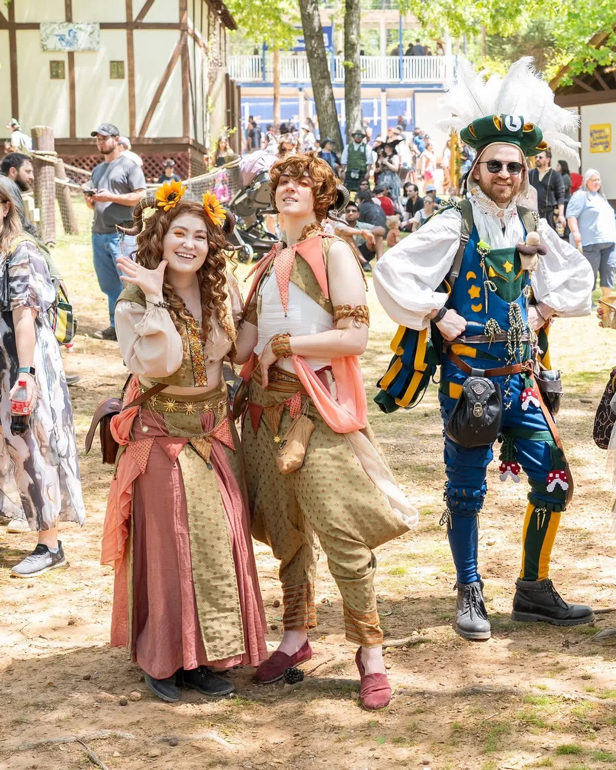 Three costumed guests posing together at the Festival &mdash; two in coordinated earth-tone fantasy outfits and one in a bright blue and green Renaissance costume.