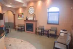 Cozy waiting room with chairs, a fireplace, wall clock, window, and neutral decor in soft lighting.