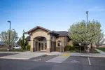 Modern beige single-story office building with arched entrance surrounded by blooming trees and parking spaces.