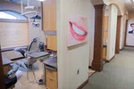 Modern dental clinic room with dental chair, equipment, and smiling teeth wall art in a clean hallway.